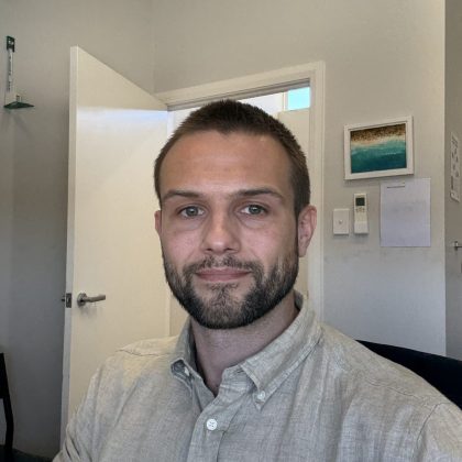 Dr Tom Blaszczyk smiles at the camra. He is wearing a neutral button up shirt and has short dark hair.